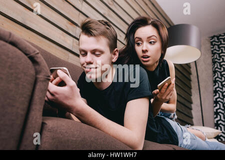 junges Paar im Bett liegend. Einer von ihnen telefonieren und flirten. andere Person ist eifersüchtig und Spione. Konzept von Eifersucht und Misstrauen. Stockfoto