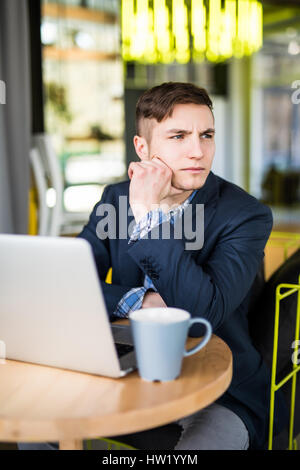 Männlichen Freiberufler verbinden mit WLAN über Laptop-Computer, nachdenklich Geschäftsmann Arbeit auf Net-Book beim Sitzen am Holztisch in modernen Kaffee-sho Stockfoto