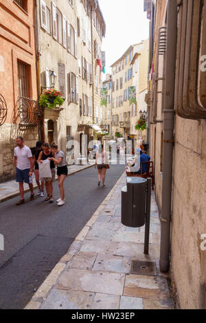 Touristen und Einheimische in einer charmanten Straße in Grasse, Provence, Frankreich. Hochhäuser bieten Schatten von der heißen Sonne in dieser Stadt, eingebettet in den französischen Alpen. Stockfoto