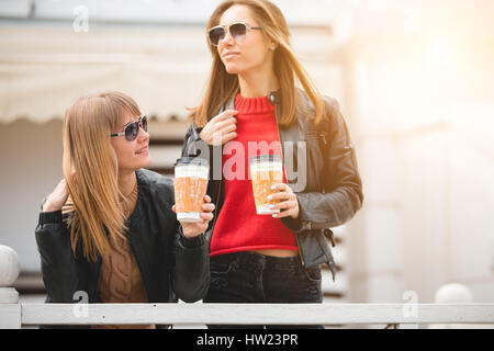 Porträt von zwei schönen jungen Freundinnen auf der Straße Pappbecher Kaffee in Händen halten. Stockfoto