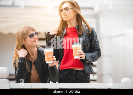 Porträt von zwei schönen jungen Freundinnen auf der Straße Pappbecher Kaffee in Händen halten. Stockfoto