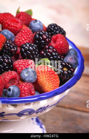 Sommerfrüchte in blau und mit Keramik Obstschale, mit einer Auswahl an Heidelbeeren, Himbeeren, Erdbeeren und Brombeeren. Stockfoto