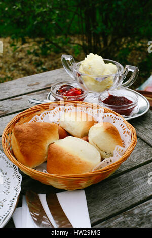 Nachmittagstee - Obst frisch gebackene Scones, Clotted Cream und Marmelade - auf einem Holztisch in einem Garten an einem sonnigen Tag. Stockfoto