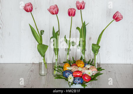 Ostern-Hintergrund mit Ostereiern und rosa Tulpen in Glasflaschen auf hölzernen Hintergrund Stockfoto