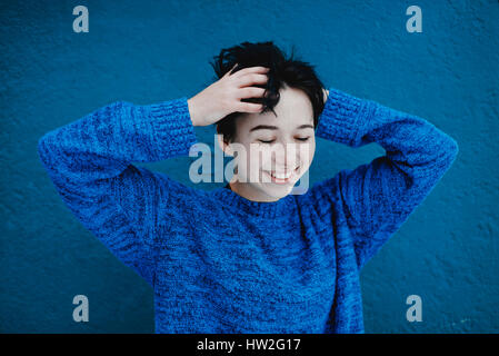 Lächelnd kaukasischen Frau umspielte Haare in der Nähe von blauen Wand Stockfoto