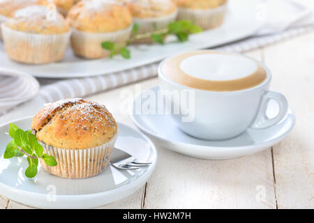 Frisch gebackene Schoko-Bananen-Muffins mit Puderzucker serviert mit einer Tasse cappuccino Stockfoto