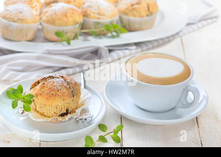 Frisch gebackene Schoko-Bananen-Muffins mit Puderzucker serviert mit einer Tasse cappuccino Stockfoto