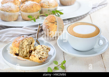Frisch gebackene Schoko-Bananen-Muffins mit Puderzucker serviert mit einer Tasse cappuccino Stockfoto