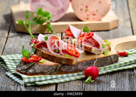 Scheiben vom Bayerischen Wurst auf Bauernbrot, garniert und serviert auf einem rustikalen Holzbrett Stockfoto