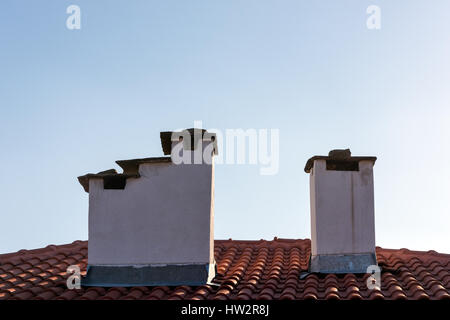 Altmodische weiße Schornsteine auf rotes Ziegeldach gegen blauen Himmel Stockfoto