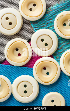 Konzept mit Beige monophonen Tasten auf farbigen Stoffstücken nah oben, Makro, Draufsicht, flach lag. Stockfoto