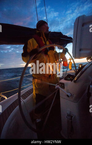 Reifer mann Lenkrad auf Segelyacht in Meer bei Sonnenuntergang Stockfoto
