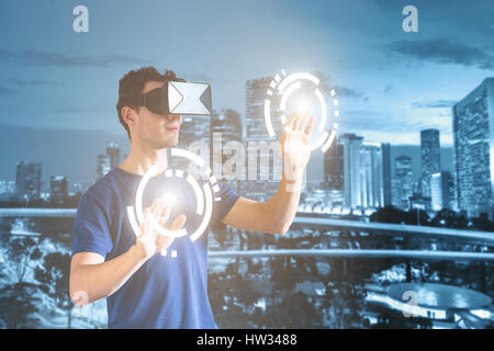 Doppelbelichtung einer Person tragen, virtuelle Realität (VR) Kopfhörer oder Gläser und berühren die Tasten mit einem modernen Stadtbild Stockfoto