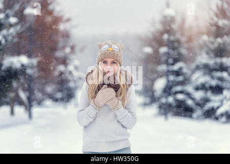 Attraktive junge blonde Mädchen im Winterwald wandern. Hübsche Frau im Winter im Freien. Winterkleidung zu tragen. Gestrickte Pullover, Schal, Mütze und mit Stockfoto