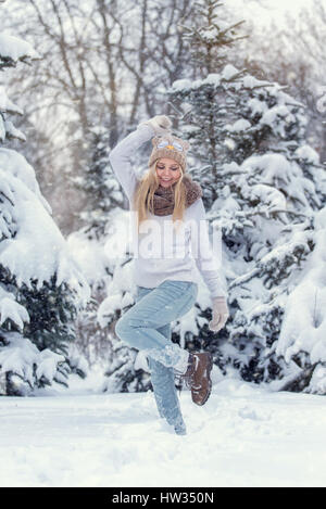 Attraktive junge blonde Mädchen im Winterwald wandern. Hübsche Frau im Winter im Freien. Winterkleidung zu tragen. Gestrickte Pullover, Schal, Mütze und mit Stockfoto