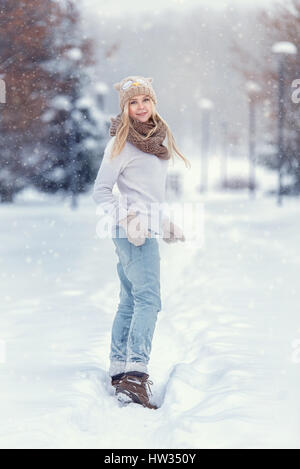 Attraktive junge blonde Mädchen im Winterwald wandern. Hübsche Frau im Winter im Freien. Winterkleidung zu tragen. Gestrickte Pullover, Schal, Mütze und mit Stockfoto