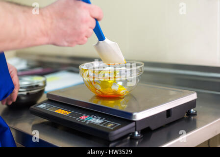 Man wiegt Karamell in eine Glasschüssel auf eine elektronische Waage Stockfoto