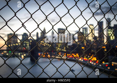 New York City Skyline Nachtlichter gesehen durch einen Zaun auf die Manhattan Bridge NYC Stockfoto