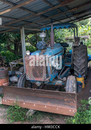 Schmutzige alte Traktor unter einem Schuppen auf dem Hof geparkt Stockfoto