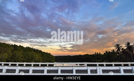 Seitenansicht der Brücke überqueren einen Baum gesäumt Spiegel wie Fluss einen dramatischen Sonnenuntergang. Stockfoto