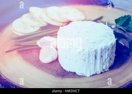 Gewürzte cremige Weichkäse mit Knoblauch und feinen Kräutern auf einer Holzplatte mit Crackern. Stockfoto