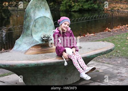 Kleines Mädchen, Kind, Kind Spaß sitzen Brunnen spielen unter Blätter im Herbst im Park St. Stephen's Green, Dublin Irland Kindheit Konzept Stockfoto