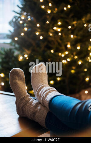 Socken von kaukasischen Frau mit Füßen auf Tisch neben Weihnachtsbaum Stockfoto