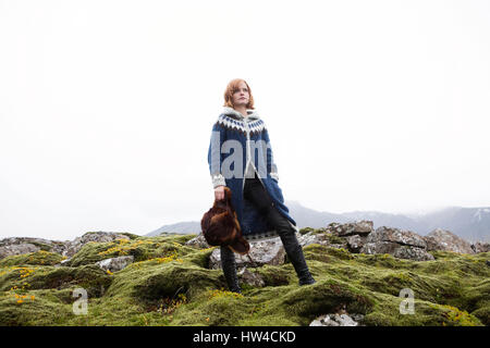 Kaukasische Frau auf bemoosten Felsen mit Pelzmütze Stockfoto