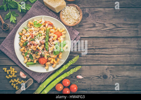 Italienische Cavatappi Nudeln mit Spargel und Tomaten auf Holztisch, Ansicht von oben mit Textfreiraum. Getönten Stockfoto