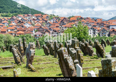 Mittelalterlichen balkan Grabsteine vor neuen Terra Cotta aufgeschlagen-Dach-Häusern. Die Grabsteine stehen an der serbischen orthodoxen Kirche St. Peter (Petrova Crkva) in Rasa, in der Nähe von Novi Pazar, Serbien.  Es ist ein UNESCO-Weltkulturerbe, mit Stiftungen aus dem Stockfoto