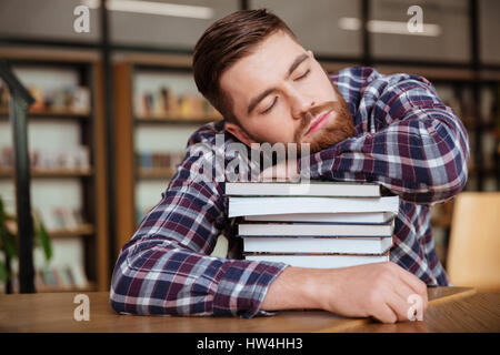 Junge müde männlichen Studenten ein Nickerchen auf einem Stapel Bücher in der Bibliothek Stockfoto