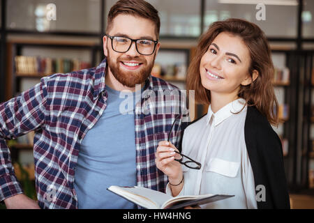 Zwei glückliche junge Studenten studieren zusammen in der öffentlichen Bibliothek und Blick in die Kamera Stockfoto
