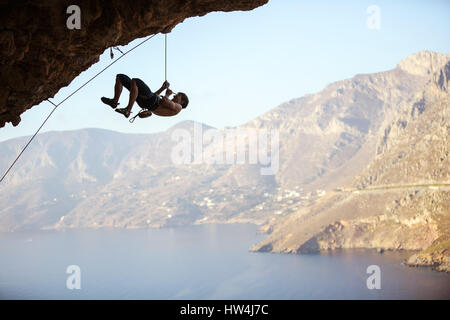 Junger Mann versucht, Klippe zu erreichen, um auch anspruchsvolle Route zu klettern. Kletterer selbst hochziehen und Seil locker zu schaffen, so dass belay Stockfoto