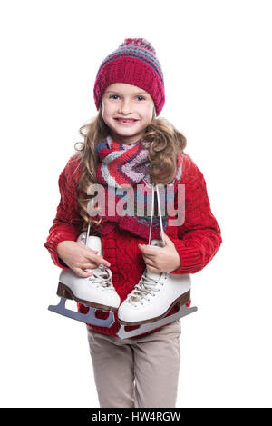 Niedliche kleine lächelnde Mädchen mit lockige Frisur tragen gestrickte Pullover, Schal, Mütze und Handschuhe mit Skates isoliert auf weißem Hintergrund. Winterkleidung Stockfoto