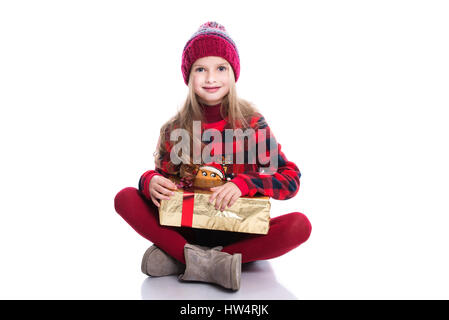 Süß lächelnd Mädchen mit lockige Frisur tragen, gestrickte Pullover, Schal und Mütze hält Weihnachtsgeschenk isoliert auf weißem Hintergrund. Winter-Tuch Stockfoto