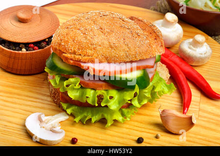 Leckere Hamburger gefüllt mit Schinken, Champignons, Gurke und frischer Salat, Knoblauch, Pfeffer Topf und Chilischote auf Schneidebrett Stockfoto