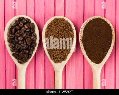 Löffel Instant Granulat und gerösteten Kaffeebohnen vor einem rosa Hintergrund Stockfoto