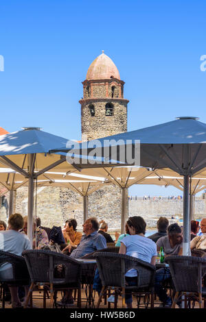 Beschäftigt Strandcafé, überragt von der Glockenturm der Kirche von Notre Dame des Anges, Collioure, Côte Vermeille, Frankreich Stockfoto