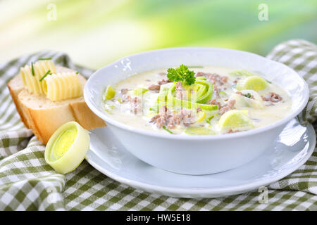 Cremige Käse-Lauch Suppe mit Hackfleisch, serviert mit Butter Baguette, Lauch im Hintergrund Stockfoto