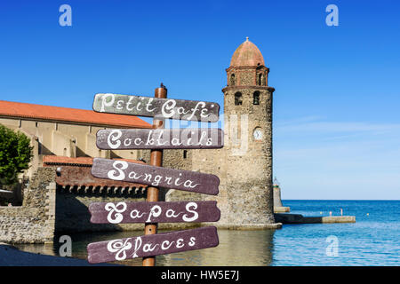 Konzentrieren Sie sich auf ein Café-Schild an ein Strandcafé, überragt von der Glockenturm der Kirche von Notre Dame des Anges, Collioure, Côte Vermeille, Frankreich Stockfoto