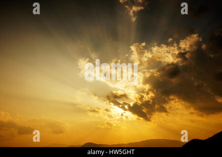 Untergehende Sonne hinter den Wolken und eine Silhouette von Bergen bei Einbruch der Dunkelheit in China. Stockfoto