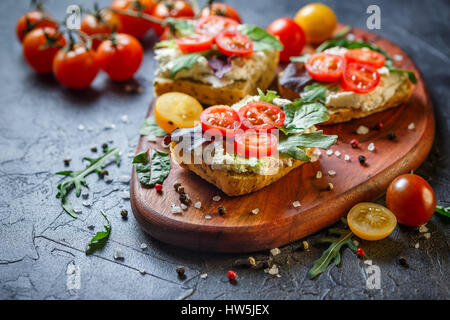 Zwei Brötchen mit Frischkäse, Cherry-Tomaten und Rucola auf ein Holzbrett. Gesunde Ernährung Stockfoto