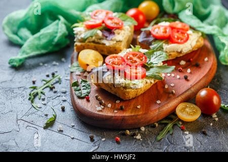 Zwei Brötchen mit Frischkäse, Cherry-Tomaten und Rucola auf ein Holzbrett. Gesunde Ernährung Stockfoto