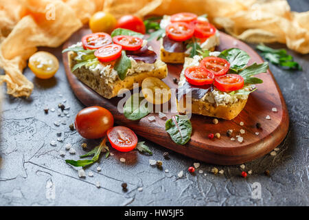 Zwei Brötchen mit Frischkäse, Cherry-Tomaten und Rucola auf ein Holzbrett. Gesunde Ernährung Stockfoto