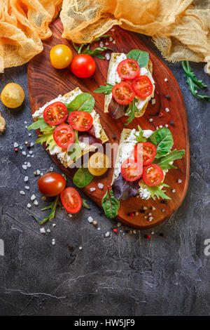 Zwei Brötchen mit Frischkäse, Cherry-Tomaten und Rucola auf ein Holzbrett. Gesunde Ernährung. Draufsicht mit Textfreiraum Stockfoto