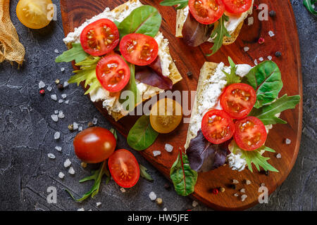 Zwei Brötchen mit Frischkäse, Cherry-Tomaten und Rucola auf ein Holzbrett. Gesunde Ernährung. Ansicht von oben. Stockfoto