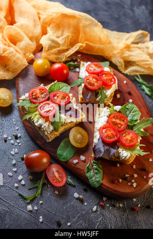 Zwei Brötchen mit Frischkäse, Cherry-Tomaten und Rucola auf ein Holzbrett. Gesunde Ernährung Stockfoto