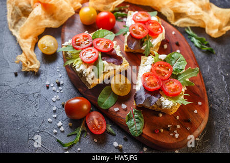 Zwei Brötchen mit Frischkäse, Cherry-Tomaten und Rucola auf ein Holzbrett. Gesunde Ernährung. Ansicht von oben. Stockfoto