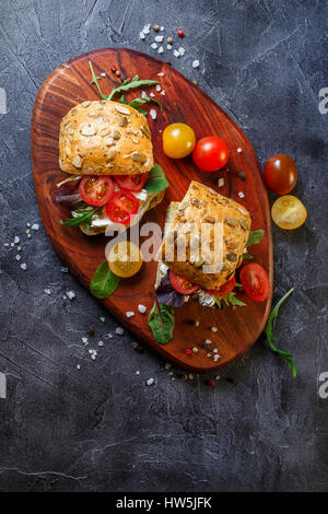 Zwei Brötchen mit Frischkäse, Cherry-Tomaten und Rucola auf ein Holzbrett. Gesunde Ernährung. Draufsicht mit Textfreiraum Stockfoto