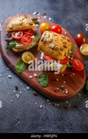 Zwei Brötchen mit Frischkäse, Cherry-Tomaten und Rucola auf ein Holzbrett. Gesunde Ernährung. Stockfoto